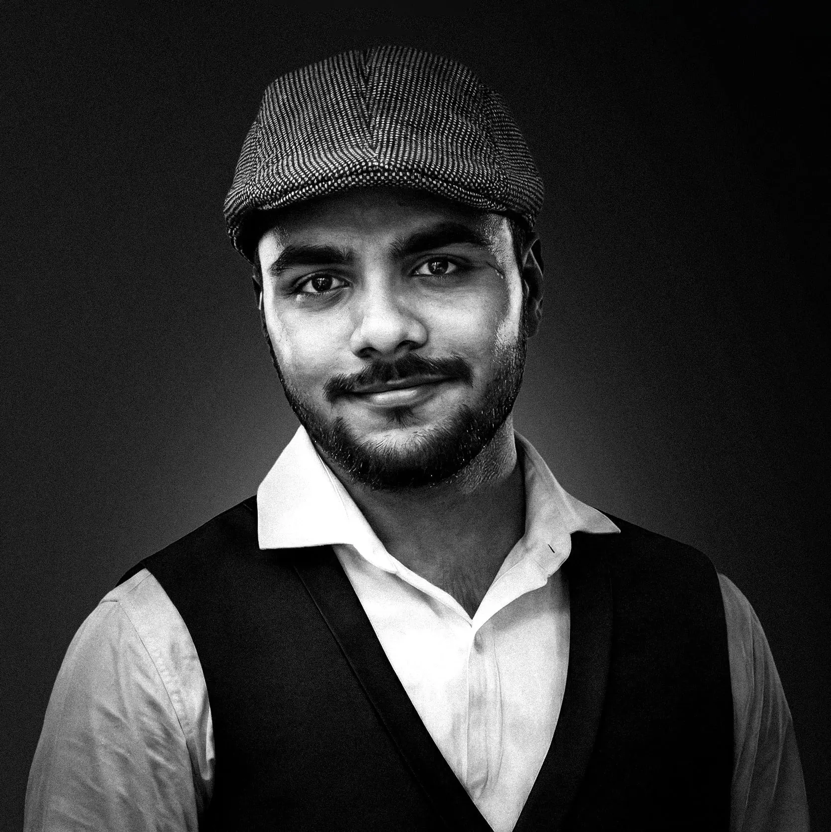 Black and white portrait of Jagesh Pandey smiling in a flat cap